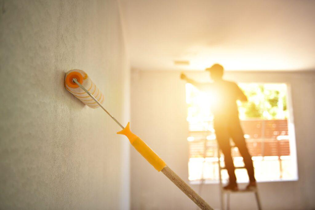  In this image, a skilled painter is seen on a ladder, using a paint roller to apply paint to the ceiling. The focus is on the painter and the roller in the foreground, while the background shows the painted ceiling. This image showcases the expertise and attention to detail that Pro-Painting brings to their interior painting services.